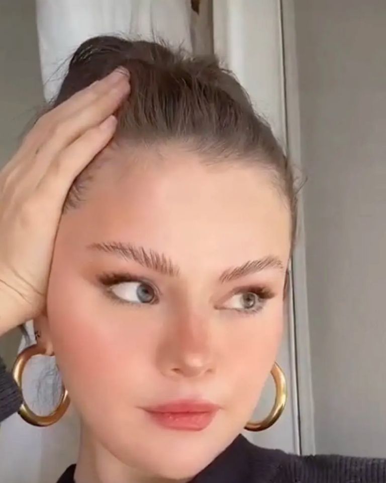 Selena Gómez con cabeza apollada en la mano y aros de argollas de color dorado, usa un filtro que cambia su cara por la de Bella Hadid